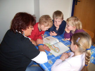 Manuela Cotterrell mit 4 Kindern am Tisch. Sie liest aus einem Buch vor.